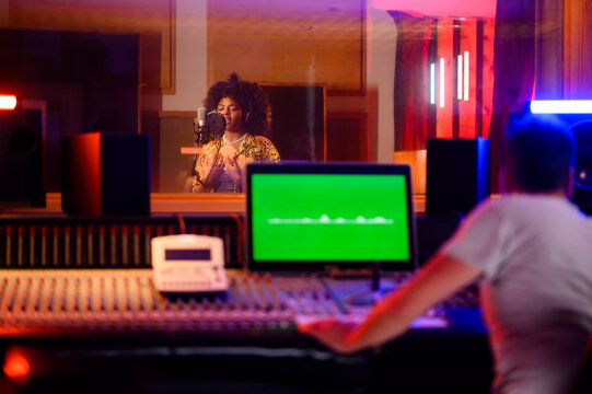 Talented multicultural singer recording in vocal isolation booth in music studio.
