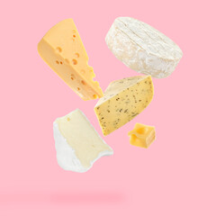 Different kinds of cheese falling on pink background