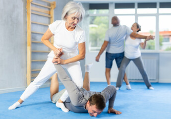 Senior woman train in pair with middle-aged coach to strike and reflect blows of enemy. Intense...