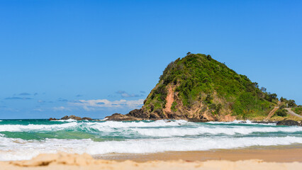 Australian coast, big rock on the seashore with blue water with waves and sandy beach, view from the beach to the seaside landscape on a summer sunny day.