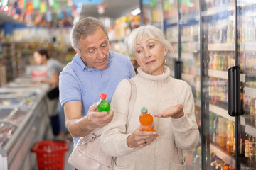 Elderly couple choosing sweet sodas together in the grocery section of a supermarket