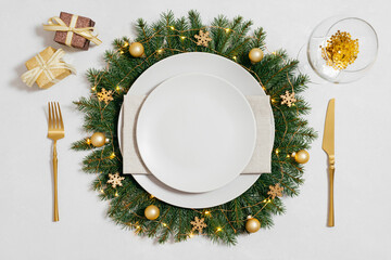 Christmas table setting with golden decorations and empty beige plate on white background. New Year table setting. Top view, flat lay.