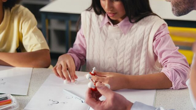 Male secondary or high school teacher helping female high school student to build model of molecule or atom in science class - shot in slow motion