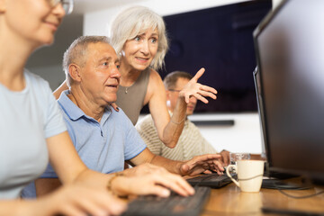 Elderly people help each other learn how to use computer. Woman suggests right decision to an mature man