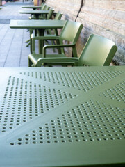 Empty plastic tables in a cafe. Green chairs and tables outside. The concept of no customers.