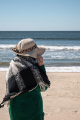 Old woman walking on the beach on a cold sunny day. Contemplating the sea.