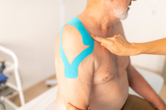 A female physiotherapist cheks the neuromuscular bandage or kinesiology tape from the shoulder of her patient, an older man