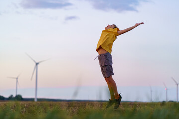 Boy in yellow shirt delight leaping into air. The backdrop features silhouetted wind turbines with...