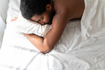Young African American man sleeping soundly in his comfortable bed at home, lying on stomach,...