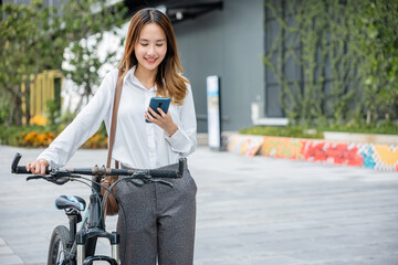 Obraz na płótnie Canvas Asian businesswoman standing on city street building with bicycle holding smart mobile phone, lifestyle smiling young woman commute with her bicycle and use smartphone at urban for work social media