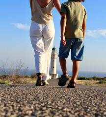 Mother and son walking towards Cap de Barberia's lighthouse, which stands beautiful on background, Formentera, Balearic Islands, Spain.