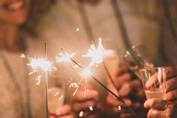 group of four people having fun and enjoying holding glasses of champagne and sparklers celebrating...