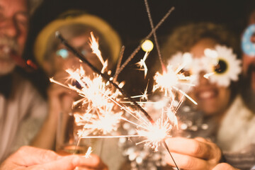 group of four people enjoying new year night celebrating with sparklers in the middle and looking at the camera - adults having fun together - obrazy, fototapety, plakaty