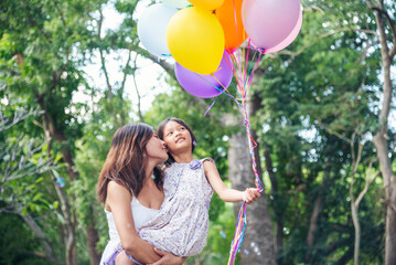 Happiness mother daughter play balloons together in green garden park outdoor lifestyle. Happy family two people enjoy have fun cheerful smile. Mother childhood hand holding colorful balloons outside