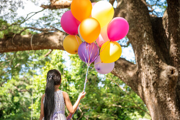 Cheerful cute girl holding balloons running on green meadow white cloud and blue sky with...