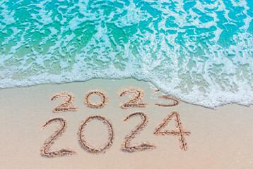 Message Year replaced by 2023 2024 written on beach sand background. Good bye 2023 hello to 2024 happy New Year coming concept.  top view - obrazy, fototapety, plakaty