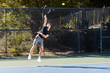 Active tennis player playing a game on an outdoor court. The man is wearing gray shorts and a black tee shirt holding a racquet. 