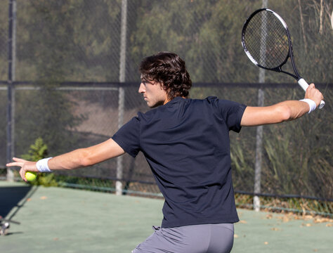 Athletic man playing tennis on a court outside. 
