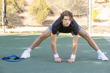 Adult male tennis player warming up and stretching before a match on the court. The man is athletic and fit ready for the action of the game. 