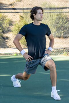 Adult male tennis player warming up and stretching before a match on the court. The man is athletic and fit ready for the action of the game. 