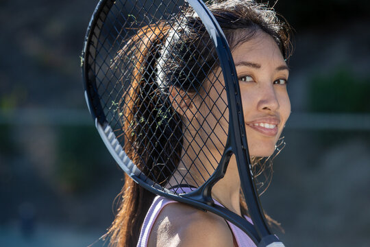 Asian female tennis player holding a racket and standing on the court outside. 