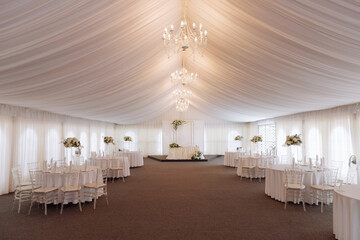 White tent with tables with white tablecloths for a wedding.