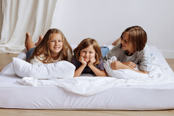 Sisters lying on a bed in their home, smmiling for the camera. High quality photo
