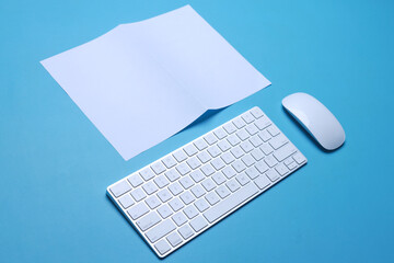 Blank white bifold paper sheet for mock up with keyboard computer and wireless mouse on a blue...
