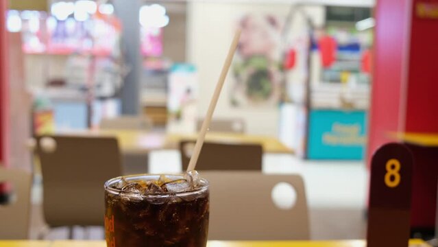 Glass with cola and ice then a white straw, queue card number, and a shop in a super supermarket and Beverage.