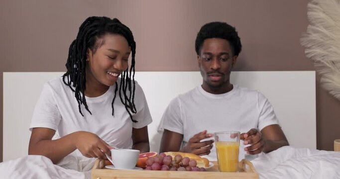 Happy afrcan american woman and man husband and wife sitting in bed awaking eating having breakfast in bed befor hard work day.