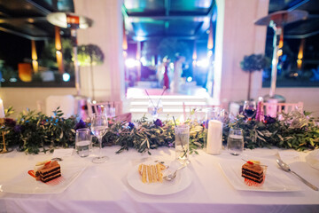 Pieces of white and chocolate cakes lie on plates on a festive table near glasses of water