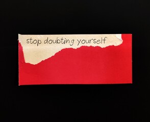 Torn red note with handwritten text STOP DOUBTING YOURSELF, concept of self-doubt, lack of...