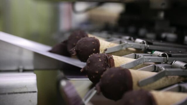 Food industry and technology. Closeup view of a commercial packaging machine wrapping ice cream cones coated in chocolate and peanut in a plastic pack. 