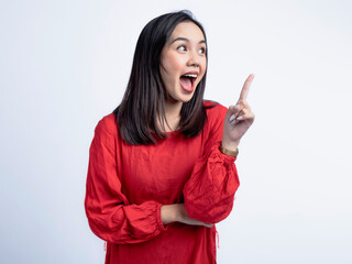 A portrait of a happy Asian woman wearing a red shirt, posing with an idea, pointing upwards. Isolated against a white background.