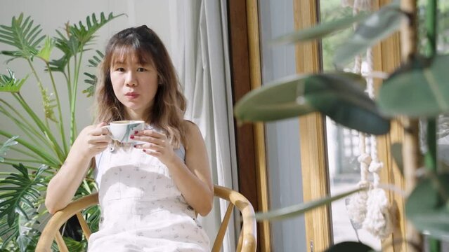 Young Asian woman enjoy hot latte in the morning while sitting in cafe with green plant background.