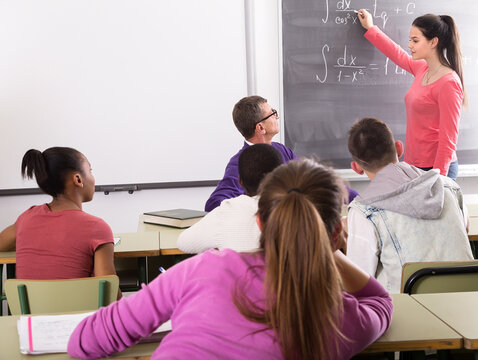 Cute student girl solves task near blackboard in classroom mathematics