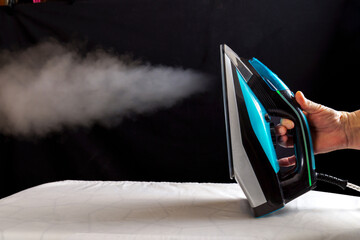 Woman ironing a white cloth by pouring steam from the iron on a black background. - obrazy, fototapety, plakaty