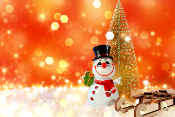 Christmas banner with bokeh and place for text. Snowman with wooden sleigh and Christmas tree on artificial snow with red background.