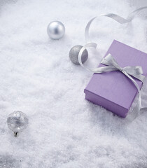 a purple gift box with a silver ribbon and silver ball on the snow