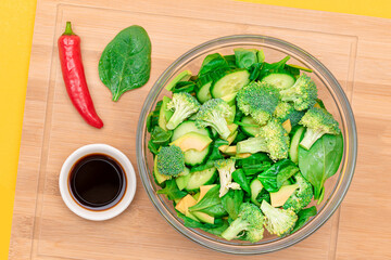 Fresh Green Salad of Avocado, Broccoli, Spinach and Cucumber with Soy Sauce and Red Hot Pepper on Wooden Cutting Board. Vegan Salad. Vegetarian Culture. Raw Food. Healthy Eating and Vegetable Diet