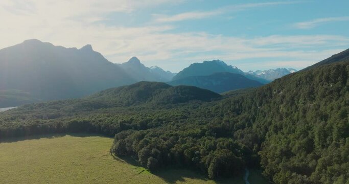 Reverse aerial drone view of tree covered landscape of rugged, wild and remote Southern Alps mountain ranges in Glenorchy, New Zealand Aotearoa