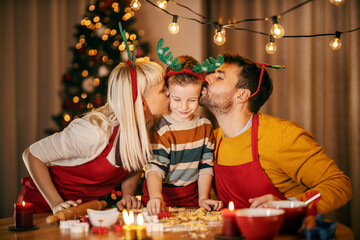 Parents kissing their son while making gingerbread cookies at home on christmas eve.