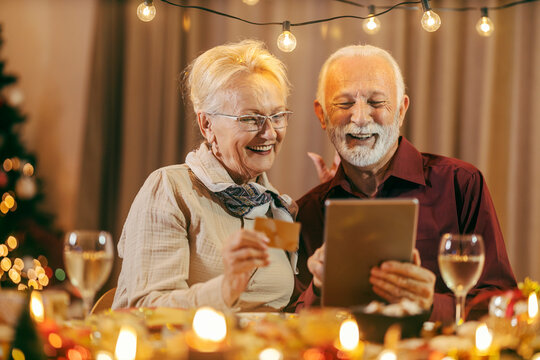 Christmas shopping. A senior couple sitting at table at home on Christmas and new year's eve and using tablet and credit card.