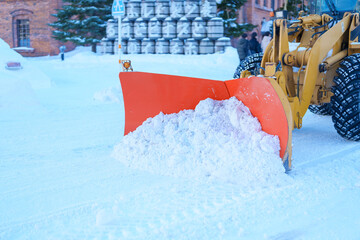 Yellow tractor removes snow from the road and clears the sidewalk in winter season. Cleaning and...