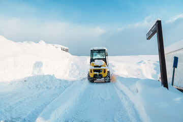 Yellow tractor removes snow from the road and clears the sidewalk in winter season. Cleaning and...