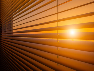 The setting sun shines through the closed horizontal blinds.