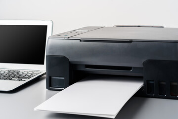 Printer and laptop on grey table in office