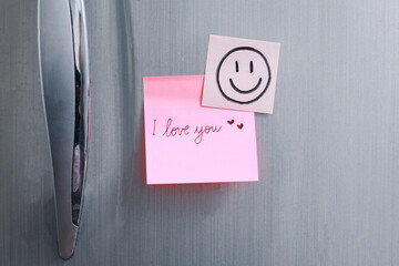 Sticky note with handwritten text I Love You attached to refrigerator door in kitchen. Romantic...