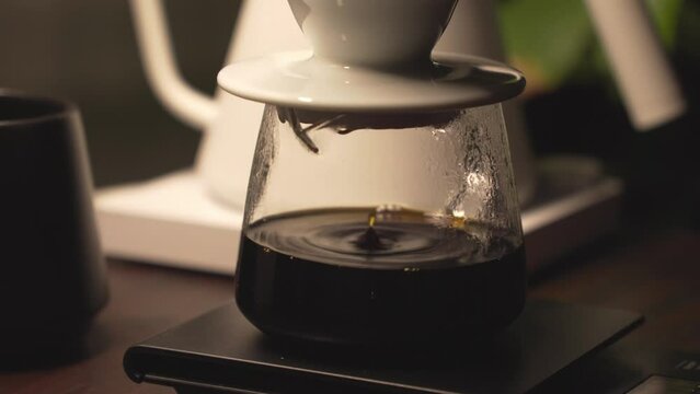 Fresh brew of black coffee drip into glass carafe through ceramic dripper