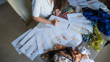 A woman draws sketches of swimwear and underwear with a pencil.